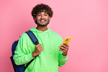 Portrait of cheerful indian student in green hoodie wear behind rucksack and using new iphone 15...