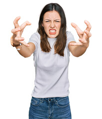 Young beautiful woman wearing casual white t shirt shouting frustrated with rage, hands trying to...