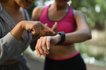 Two sporty women checking their fitness trackers on smartwatch after outdoor training