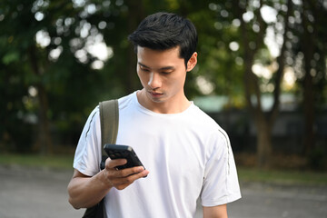 Attractive sporty man with backpack using mobile phone at a city park