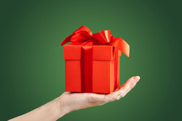 Hand with red gift box with red bow isolated green background copy space new year concept