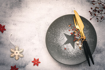 Ein weihnachtlicher Teller mit Essbesteck auf einem grauen Tisch. Draufsicht.
