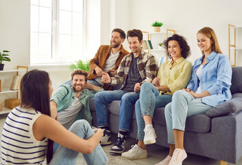 Group of a happy young friends men and women sitting on sofa in the living room at home discussing and talking with each other enjoying meeting. Friendship, party and home leisure concept. - obrazy, fototapety, plakaty