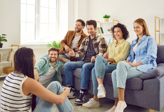 Group of a happy young friends men and women sitting on sofa in the living room at home discussing and talking with each other enjoying meeting. Friendship, party and home leisure concept.