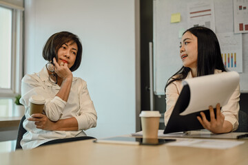 Senior female mentor listening attentively to young female employee talking at group office meeting