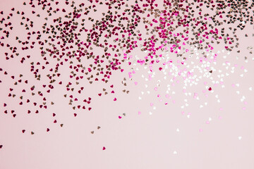 Greeting background with empty space. Violet sparkle sequins, glitter in heart shape on a gentle pink background. Top view