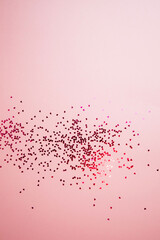 Greeting background with empty space. Violet sparkle sequins, glitter in heart shape on a gentle pink background. Top view