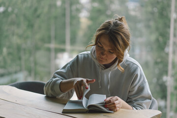 A Woman reads the book and drinks coffee from a thermos cup near the beautiful panoramic window...