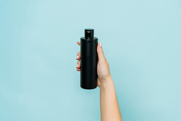 Woman's hand holding black bottle of cosmetic product for shower on blue background