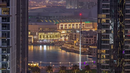 Deurstickers Aerial view of Dubai Fountain in downtown with palms in park next to shopping mall and souq day to night timelapse, UAE © neiezhmakov