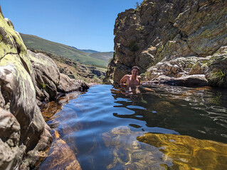 Jovem a desfrutar de um charco a meio de um curso de água pelas rochas abaixo na natureza em Fisgas de Ermelo, Portugal