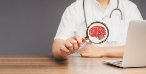 Doctor holding a magnifying glass with a brian icon while sitting at a desk in the hospital