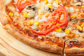 delicious pizza with chicken, mushrooms, cheese, tomatoes and corn on a wooden background