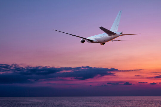A large wide body passenger airplane takes off over the sea against the backdrop of a picturesque sunset sky