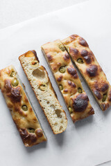 cutting homemade olive focaccia on a white countertop, Flatlay of focaccia with green olive topping, fresh homemade focaccia bread