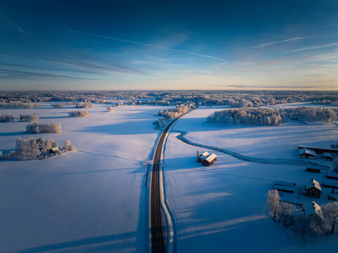 Winter Wonderland Sunrise: Majestic Aerial View of a Swedish Landscape with a Serene Roadway Cutting Through the Frozen Beauty