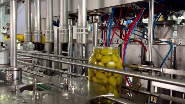 Olives in glass containers move on the production line. Factory for the production of canned vegetables and juices. Glass jar with green olives on the conveyor belt of a cannery.