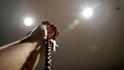 A rosary and it's cross are held in one hand, with dramatic lights on an isolated background 