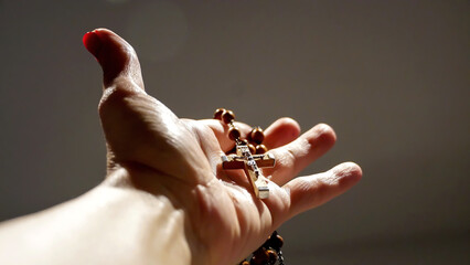 A rosary and it's cross are held in one hand, with dramatic lights on an isolated background 