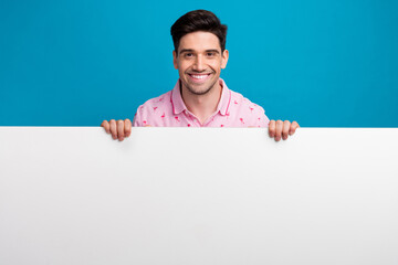 Photo of nice cheerful young man beaming smile demonstrate empty space billboard isolated on blue color background