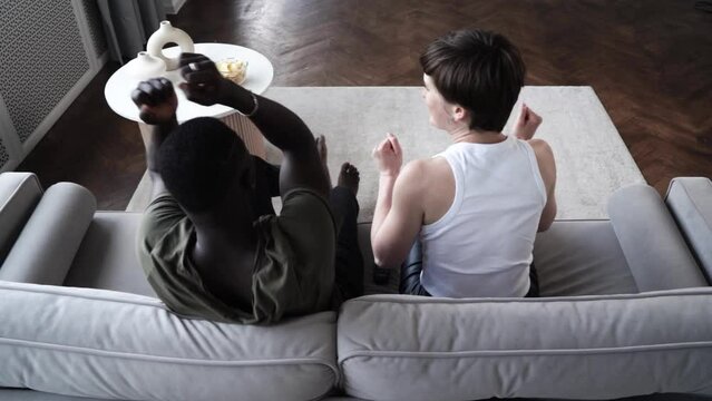 Young afroamerican man and caucasian woman watching TV, aeting chips