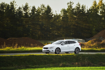 Car speeding in the countryside. Driving fast on a road surrounded by greenery in a modern hatchback. Side view of modern hatchback moving on the highway. - obrazy, fototapety, plakaty