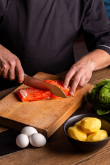 Close-up of dressed in black chef cuts with knife the salmon at the professional kitchen.
