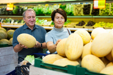 Senior married couple buy ripe melon in supermarket