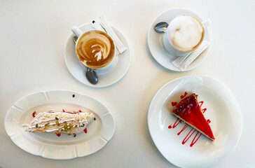Two cups of cappuccino and cake on a white table