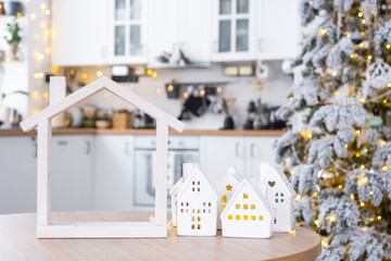 Cozy Christmas decor tiny house of small size on table of festive white modern kitchen. Gift for New Year. Insurance, moving to new house, mortgage, rent and purchase real estate - obrazy, fototapety, plakaty