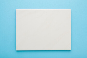 New light gray ceramic tile on light blue table background. Pastel color. Closeup. Top down view. Empty place for text.