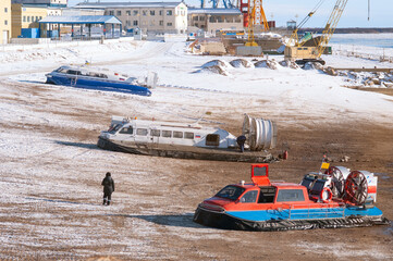 Three hovercraft on the shore of a passenger international river port on a winter sunny day. Snow and mud.