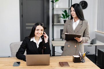 Call center agent with headset working on support hotline in modern office. Two young attractive women are working in the office