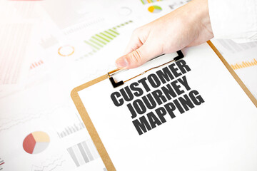 Text CUSTOMER JOURNEY MAPPING on white paper plate in businessman hands with financial diagram....