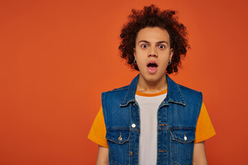 young shocked handsome african american man with accessories looking at camera on orange backdrop