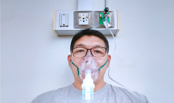 Asian adult man with asthma and respiratory diseases using nebulizer mask in inhalation therapy at hospital, front view 