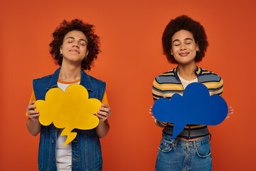 good looking african american brother and sister posing with thought bubbles on orange backdrop