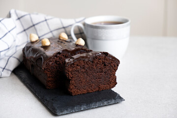 Healthy carob cake sugar free gluten free. Chocolate pound cake on slate board with kitchen towel and cup of tea or coffee. Homemade bakery. Healthy dessert.