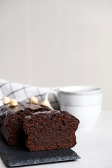 Chocolate pound cake with chocolate ganache on slate board with kitchen towel and cup of tea or coffee. Homemade bakery dessert, classic recipe of chocolate loaf cake.