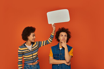 pensive african american siblings in casual attire posing with speech bubble on orange backdrop