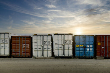 Row of multiple stacked shipping containers in a line formation with a sunrise in the background