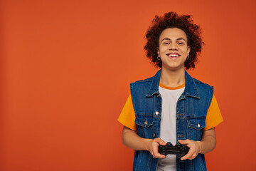 young handsome african american man emotionally playing video games with joystick on orange backdrop