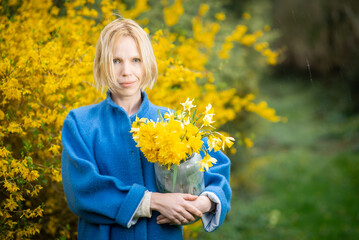 A yellow bouquet of flowers on a background of yellow flowers in a woman's hands. A middle-aged woman in a blue coat.