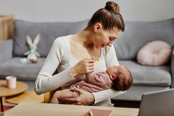 Side view of smiling Caucasian woman holding newborn in arms and giving pacifier to baby while...