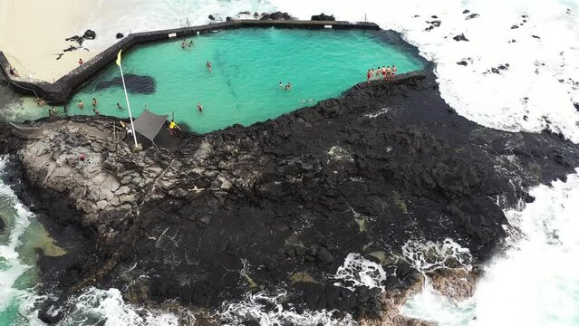 Aerial drone view of the beach of Boucan Canot with high waves crashing into the natural pool and kids having fun, Boucan Canot, Saint - Paul, Reunion.