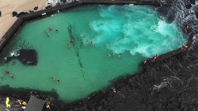 Aerial drone view of the beach of Boucan Canot with high waves crashing into the natural pool and kids having fun, Boucan Canot, Saint - Paul, Reunion.