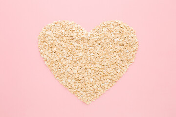 Heart shape created from dry rolled oat on light pink table background. Pastel color. Love healthy food. Closeup. Top down view.