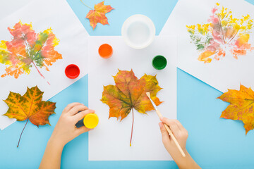 Little child hands painting and copying colorful leaves pattern with gouache color on white papers....