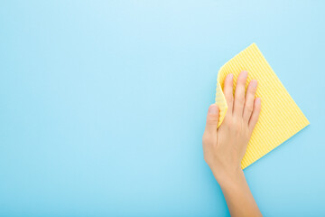Woman hand holding yellow sponge cloth and wiping table, wall or floor surface in kitchen, bathroom or other room. Closeup. Empty place for text. Light blue background. Pastel color. Top down view.