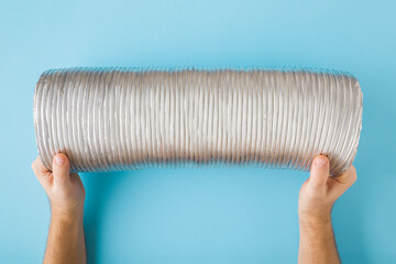 Man hands holding and showing new corrugated aluminium pipe on light blue table background. Point...